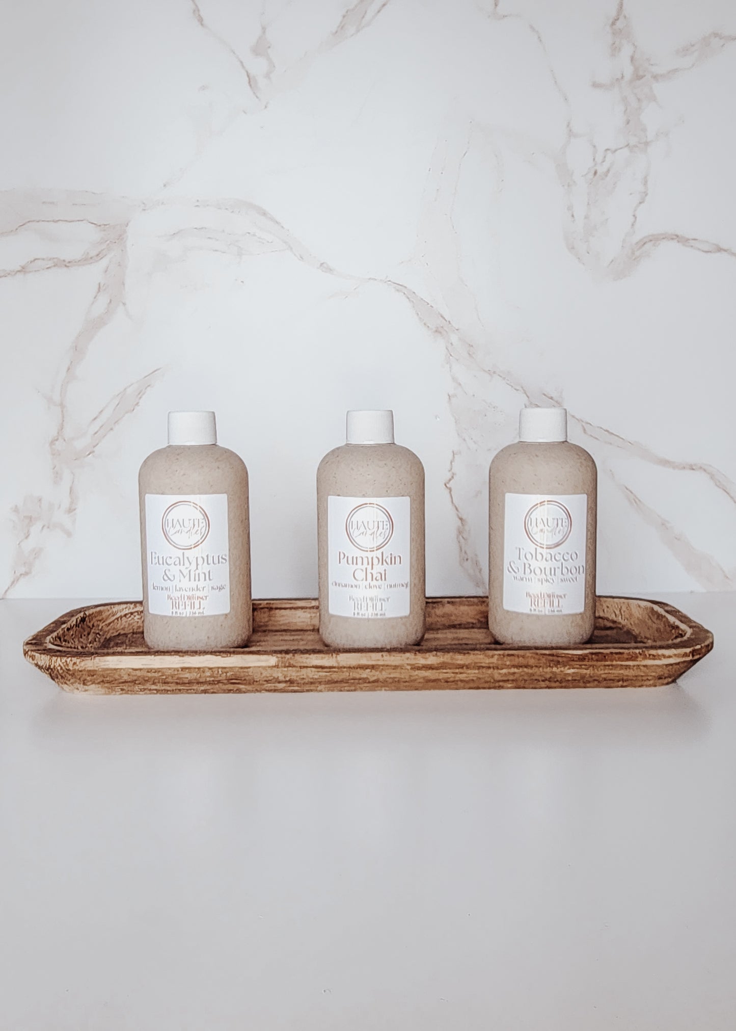 Three bottles of feed diffuser refills on a wooden tray against a marble wall.
