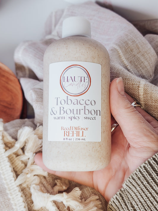 Hand holding a bottle of 'Tobacco & Bourbon' room diffuser refill with a soft, neutral background.